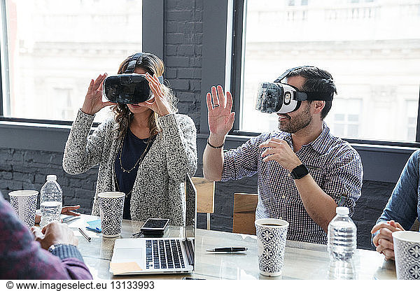 Colleagues wearing virtual reality simulator while sitting in office
