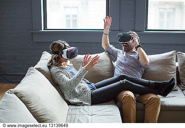 Colleagues wearing virtual reality simulators while sitting on sofa in office