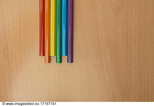 Colored pencils forming a rainbow flag on a wooden background.