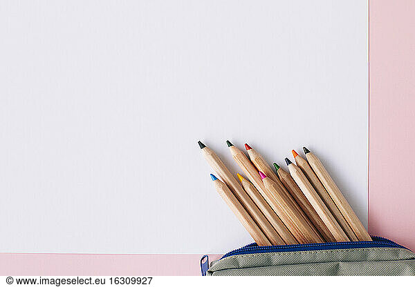 Colored pencils in pouch on blank white paper over pink background