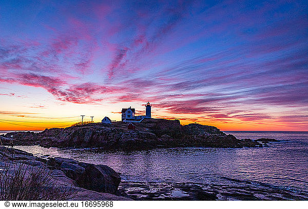 Colorful clouds above silhouetted coastal lighthouse at blue hour.