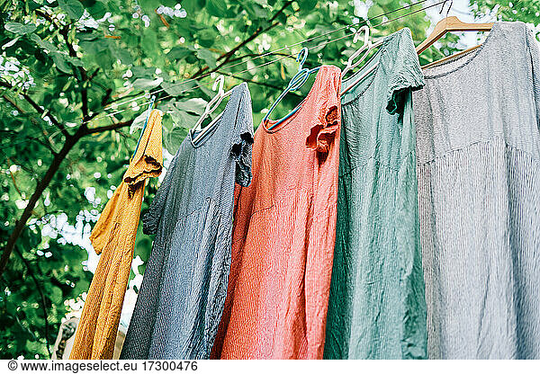 Colorful dresses hanging on hangers on the clothesline in the home garden