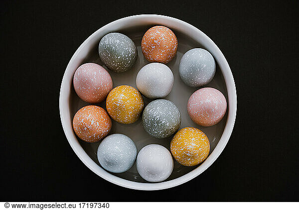 Colorful Easter eggs in white bowl on black background
