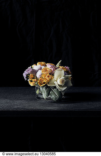 Colorful flowers in vase on table against black background