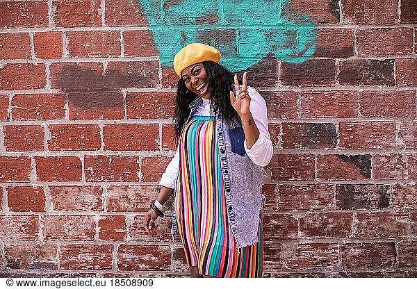 Colorfully dressed adult Black woman outside smiling with peace sign