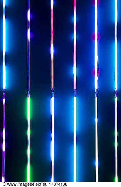 Colourful glowing striped neon lights on black wall