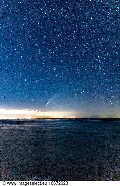 Comet NEOWISE streaking through the starry night sky above the ocean.