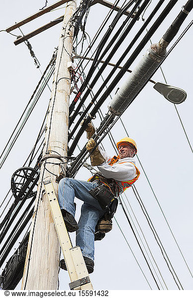 Communications worker positioning new cable on power pole