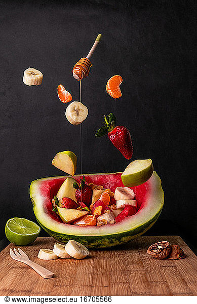 Composition of flying fruits falling on a bowl-shaped watermelon dippe