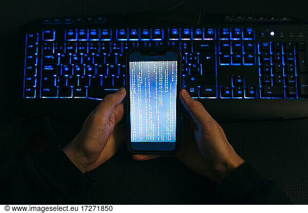 Computer Hacker Hand hält Handy gegen Computer-Tastatur im Büro