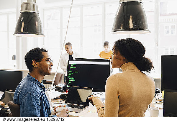 Computer hackers discussing at desk while sitting in creative office