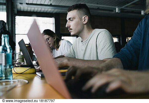 Concentrated businessman working on laptop amidst colleagues in startup company