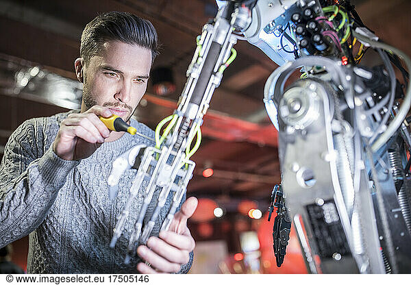 Concentrated engineer fixing robotic arm with screwdriver at workshop
