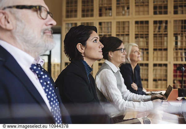 Concentrated lawyers listening in meeting while sitting at library