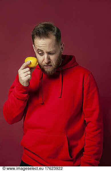 Concentrated man looking at citrus fruit against red background