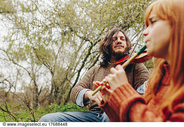 Concentrated man playing violin with woman in field