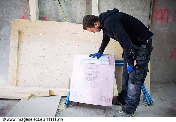 Concentrated manual worker reading blue prints at construction site