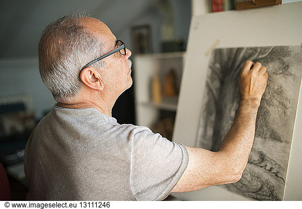 Concentrated senior man sketching on canvas at home