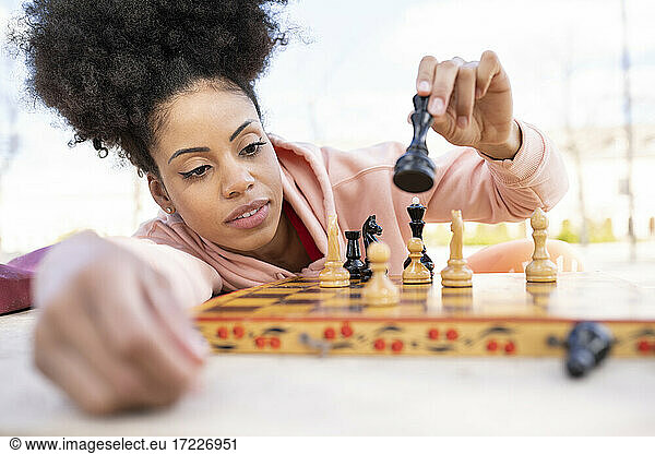 Concentrated woman playing chess while leaning on table