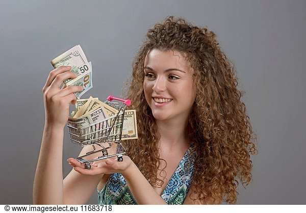 Concept of the cost of living a smiling woman holding supermarket trolley full of cash