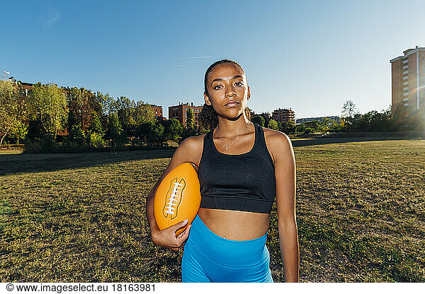 Confident American football player with sports ball in field