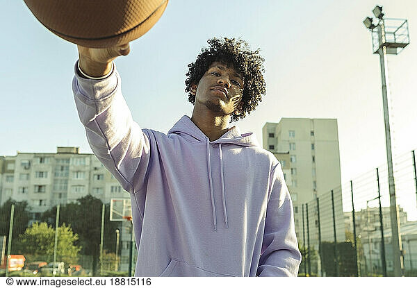 Confident athlete wearing purple hoodie holding basketball at sports court