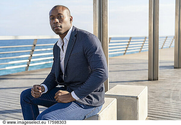 Confident bald businessman sitting on bench at promenade