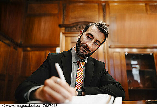 Confident bearded male lawyer signing contract document in board room during meeting