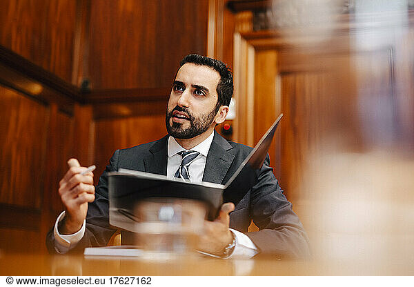 Confident bearded male lawyer with contract file sitting in board room during meeting