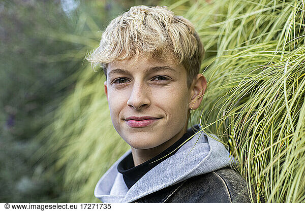 Confident blond teenage boy standing against plants