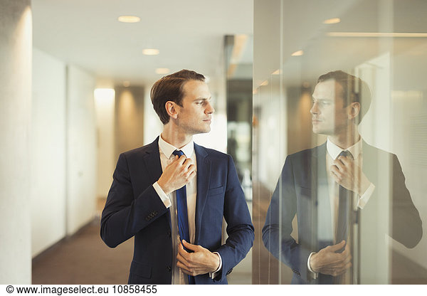 Confident businessman adjusting tie in office corridor