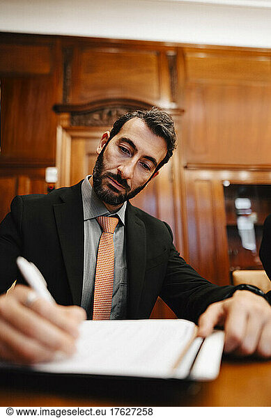Confident businessman signing contract document sitting at conference table in board room during meeting