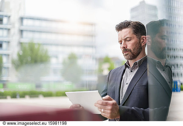 Confident businessman using digital tablet while standing outside office building in city