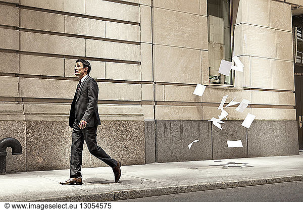 Confident businessman walking while papers flying at city street