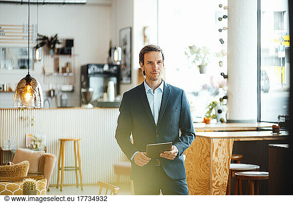Confident businessman with tablet PC standing at cafe
