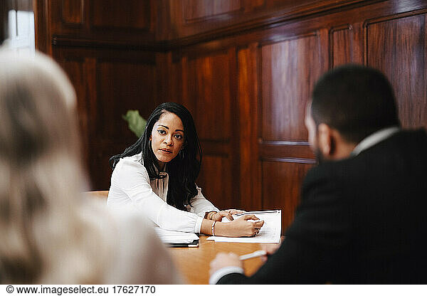 Confident businesswoman discussing over contract document with colleagues in board room