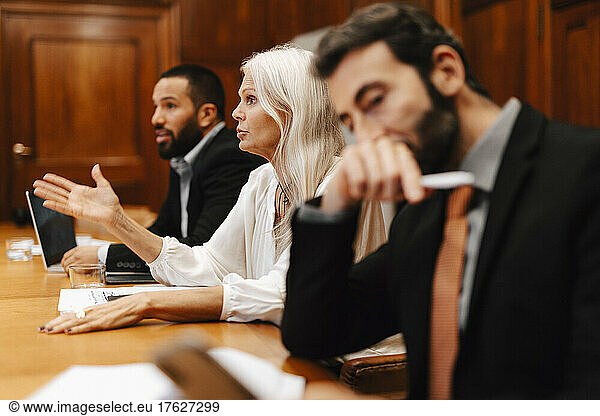 Confident businesswoman gesturing while discussing strategy amidst male colleagues in board room