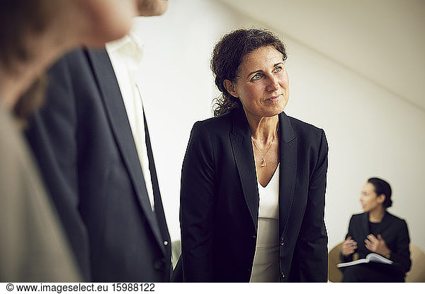 Confident businesswoman looking away while standing with lawyers at office during meeting
