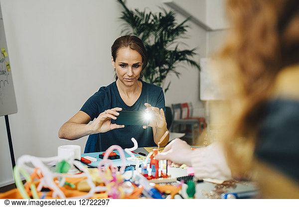 Confident businesswoman photographing stationery on table at creative office