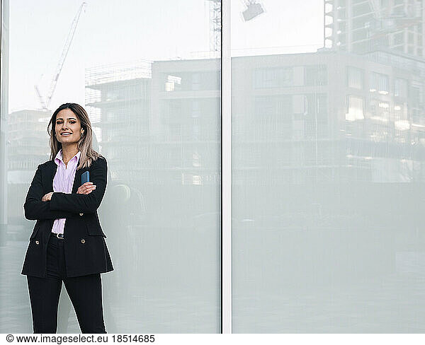 Confident businesswoman standing with arms crossed near wall