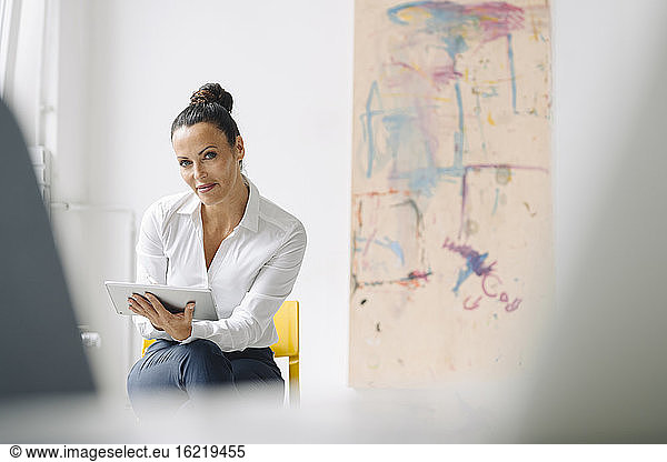 Confident businesswoman using digital tablet while sitting on chair in home office