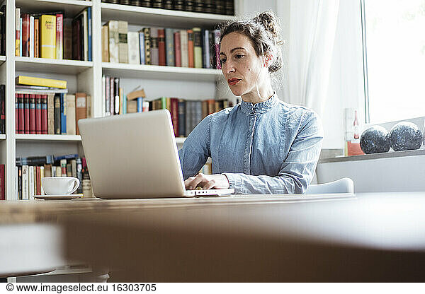 Confident businesswoman using laptop on table while sitting in cafe