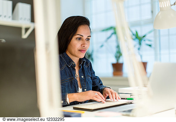 Confident businesswoman using laptop while sitting at desk in creative office