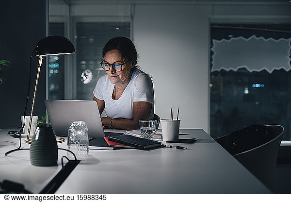 Confident businesswoman using laptop while working late night in office
