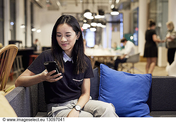Confident businesswoman using mobile phone while sitting on sofa at creative office