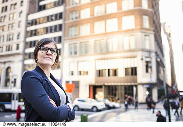 Confident businesswoman with arms crossed standing against buildings in city