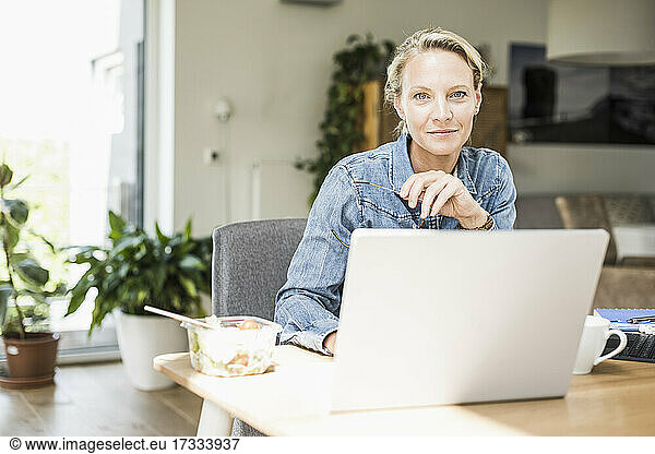 Confident businesswoman with laptop sitting at home