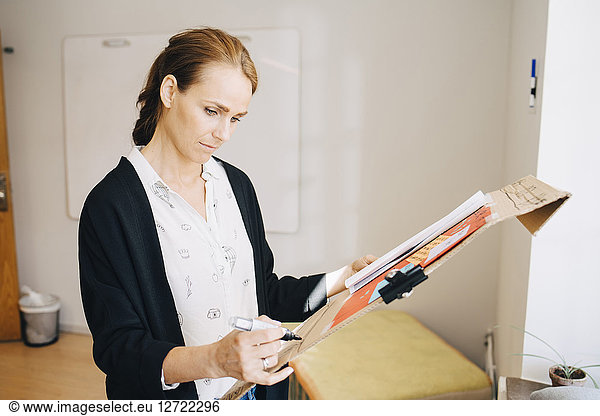 Confident businesswoman writing strategy on placard at creative office