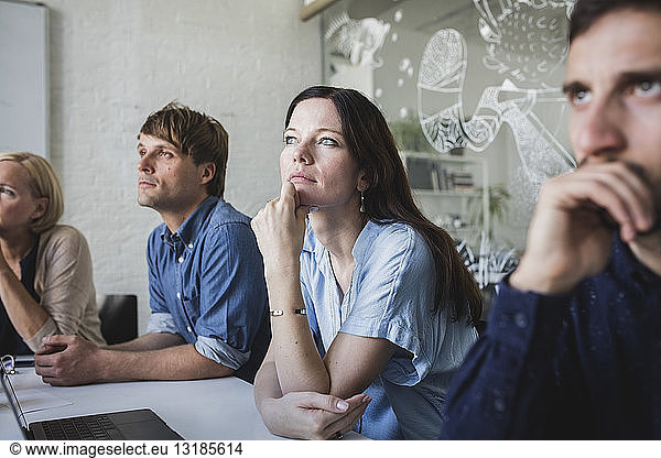 Confident creative business professionals listening while sitting in board room during meeting