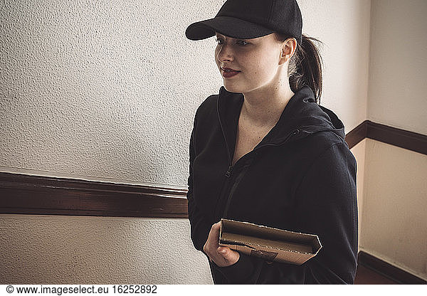 Confident delivery woman with package against wall